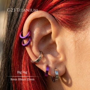 May include: G23 Titanium hoop earrings in purple and silver tones. The jewelry set includes multiple circular rings of varying sizes, specifically 18g and 16g gauges with 8mm, 10mm, and 12mm diameters, worn in the ear cartilage and lobe piercings.