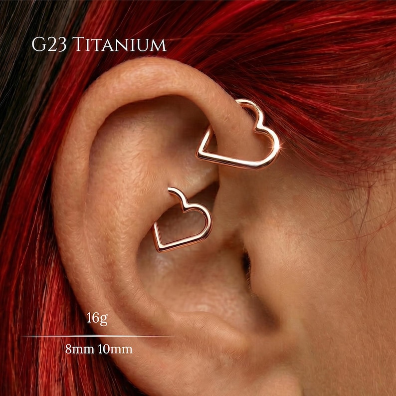 Pode incluir: Dois brincos de argola em forma de cora&ccedil;&atilde;o na cor ouro rosa feitos de tit&acirc;nio G23. A joia est&aacute; rotulada como 16g com tamanhos de 8mm e 10mm. Os brincos s&atilde;o usados na cartilagem superior e m&eacute;dia da orelha, com uma estrutura aberta.