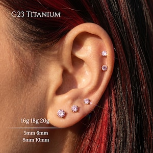 May include: An ear adorned with several small, pink gemstone stud earrings. The text "G23 TITANIUM" is visible. The image also includes the text "16g 18g 20g" and measurements "5mm 6mm 8mm 10mm".