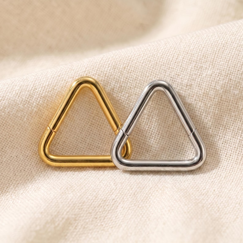 Peut inclure: Deux anneaux triangulaires, l'un dor&eacute; et l'autre argent&eacute;, avec une finition polie. Chaque anneau est dot&eacute; d'un m&eacute;canisme &agrave; charni&egrave;re, permettant &agrave; la forme triangulaire de s'ouvrir et de se fermer pour une insertion facile dans un piercing.