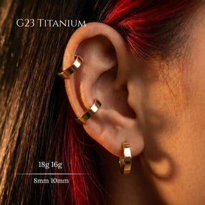 May include: Three gold-coloured hoop earrings worn on the ear, labelled G23 TITANIUM, 18g 16g, and 8mm 10mm. The jewellery consists of two cartilage hoops and one lobe hoop, all featuring a smooth, polished finish and a simple, circular design.