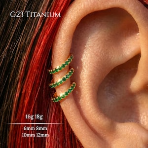 May include: Gold-colored ear cuff earrings with a row of small, green gemstones. The earrings are shown on an ear, with the text "G23 TITANIUM", "16g 18g", "6mm 8mm", and "10mm 12mm" visible.