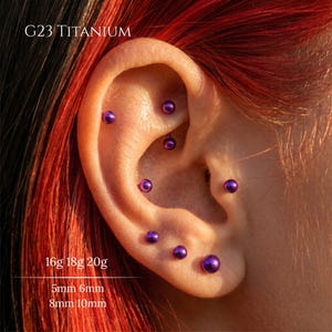 Peut inclure: Un ensemble de piercings d'oreille en titane G23 avec des embouts sphériques métalliques violets. Le texte G23 TITANIUM, 16g 18g 20g, et 5mm 6mm 8mm 10mm est visible sur l'image, indiquant le matériau, les calibres et les longueurs.