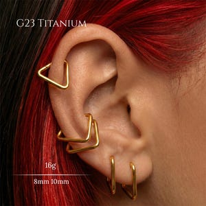 Peut inclure: Un ensemble de cr&eacute;oles triangulaires en titane G23 de couleur dor&eacute;e port&eacute;es dans plusieurs piercings d'oreille. Les bijoux sont &eacute;tiquet&eacute;s avec une &eacute;paisseur de 16g et des diam&egrave;tres de 8mm et 10mm. Finition m&eacute;tallique lisse et polie.