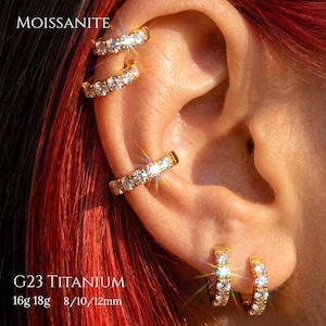 Könnte beinhalten: Goldfarbene Creolen und Ohrklemmen mit klaren, funkelnden Moissanit-Steinen. Der Schmuck besteht aus G23-Titan und ist in den Stärken 16g oder 18g mit Durchmessern von 8mm, 10mm oder 12mm erhältlich, wie im sichtbaren Text angegeben.