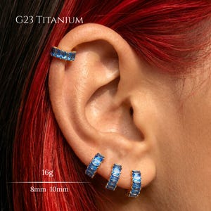 Peut inclure: Créoles en titane G23 ornées d'une rangée de pierres bleues rectangulaires. L'ensemble comprend des pièces d'une épaisseur de 16g avec des diamètres de 8 mm et 10 mm. Les boucles d'oreilles sont dotées d'un mécanisme de fermeture à charnière.