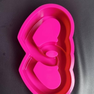 May include: A bright pink silicone mold with a unique, abstract shape. The mold features a series of curved lines and rounded sections, creating a distinctive design. The object is made of a flexible material and is likely used for baking or crafting.