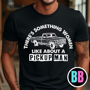 May include: Black t-shirt with white text that reads "There's something women like about a pickup man." A vintage pickup truck is pictured in the center of the text.