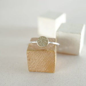Peut inclure: Une bague en argent avec un centre rond de couleur or, orné d'un motif stylisé en forme d'étoile ou de fleur.