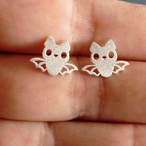 Peut inclure: Une paire de boucles d'oreilles en argent en forme de chauve-souris. Les chauves-souris ont un design mignon et cartoon avec de grands yeux.