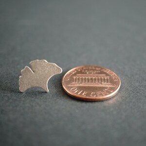 Op de afbeelding: Een zilverkleurige metalen uitsnijding van een ginkgo-blad, naast een Amerikaanse cent. De munt is koperkleurig en heeft het Lincoln Memorial en de woorden "United States of America" en "One Cent".