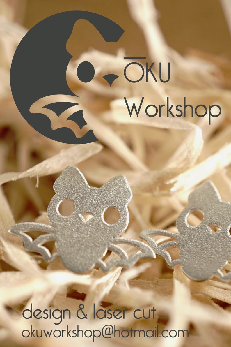 Peut inclure: Deux boucles d'oreilles en forme de chauve-souris argent&eacute;es avec des ailes et des yeux d&eacute;coup&eacute;s. Les boucles d'oreilles sont sur un lit de copeaux de bois. L'image comprend le texte "OKU Workshop" et "design & laser cut okuworkshop@hotmail.com".