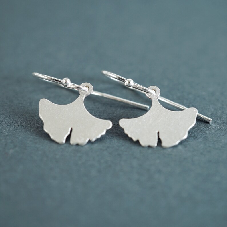 May include: A pair of silver ginkgo leaf earrings with a simple design. The earrings are made of sterling silver and have a delicate, minimalist look.