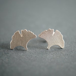 Op de afbeelding: Een paar zilveren oorbellen in de vorm van ginkgo bladeren. De oorbellen hebben een getextureerd oppervlak en zijn een eenvoudig, elegant ontwerp.