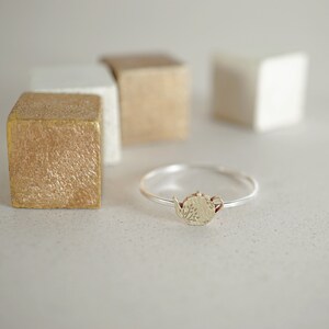 K&ouml;nnte beinhalten: Ein silberner Ring mit einem goldenen Teekannen-Anh&auml;nger. Die Teekanne hat ein florales Design.