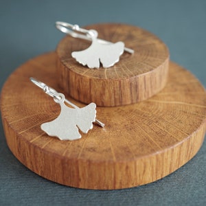 May include: A pair of silver ginkgo leaf earrings on a wooden display stand.
