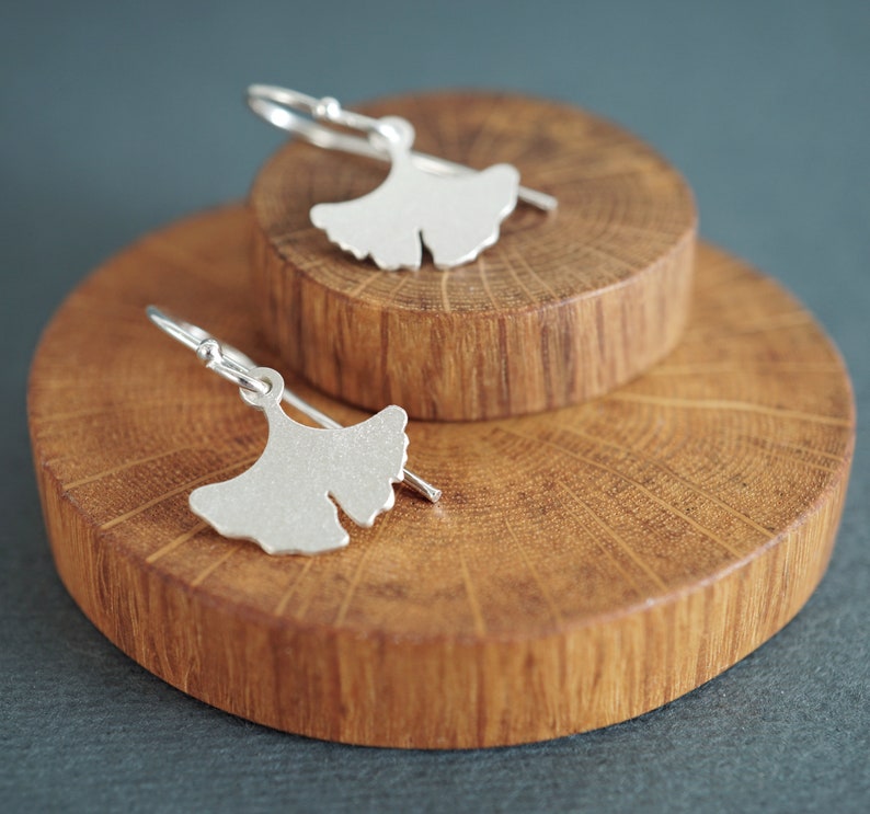 May include: A pair of silver ginkgo leaf earrings on a wooden display stand.