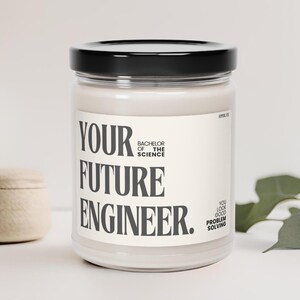 以下が含まれることがあります： 黒い蓋と白いラベルが付いた白いキャンドル。ラベルには「Your Future Engineer. Bachelor of the Science. You Look Good Problem Solving.」と書いてあります。