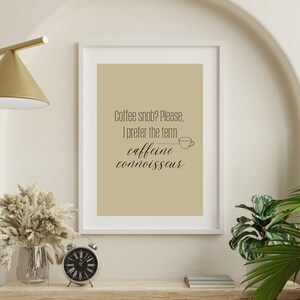 Peut inclure: Une impression murale beige imprimable avec un cadre blanc. L'impression présente une illustration en noir et blanc d'une tasse de café et le texte "Coffee snob? Please. I prefer the term caffeine connoisseur."