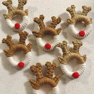 May include: Six brown and white reindeer ornaments with red pom-poms for noses. The ornaments are made of yarn and are perfect for decorating a Christmas tree.