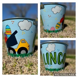 May include: A blue metal Easter bucket with a painted design of a yellow dump truck, green grass, and colorful eggs. The bucket also has the name "LINCO" painted on it in green letters.