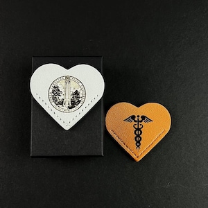 May include: Two heart-shaped leather bookmarks. One is white with the North Carolina State University seal. The other is brown with a black caduceus symbol.