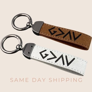 Puede incluir: Dos llaveros de cuero con un anillo de metal plateado y un cierre de metal negro. Los llaveros son marrones y blancos y presentan un símbolo "G"><"V" negro.