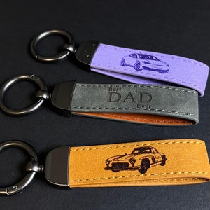 May include: Three leather keychains with metal rings. The top keychain is purple with a car design. The middle keychain is gray with the text "Best Dad Ever". The bottom keychain is brown with a car design.