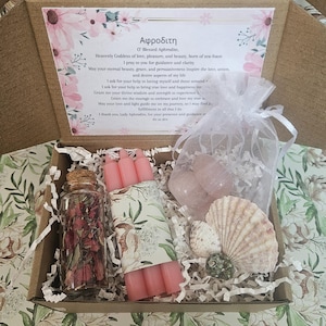 Pode incluir: Uma caixa de presente contendo um frasco de vidro cheio de p&eacute;talas de rosa secas, velas rosa, cristais de quartzo rosa e conchas. A caixa tamb&eacute;m inclui um cart&atilde;o impresso com texto em grego e ingl&ecirc;s.