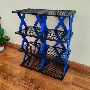 May include: A four-tier storage rack featuring black grid-patterned shelves supported by bright blue X-shaped side frames. The unit is constructed with a modular design, showcasing a vertical arrangement of four levels for organization and storage.