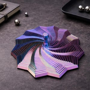 May include: A metal kinetic desk toy featuring a circular, multi-layered design with a spiraling, iridescent finish that shifts between shades of purple, blue, and pink. The object has a central vertical handle and a geometric, stepped surface.