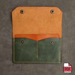 May include: A green leather wallet with two pockets and a brown leather flap. The wallet is open and the inside is visible. The wallet has two snaps on the front.