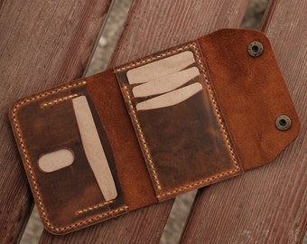 May include: A brown leather tri-fold wallet featuring visible stitching, multiple interior card slots, and two metallic snap buttons on the flap. The wallet is open, displaying its internal compartments and the textured surface of the leather.
