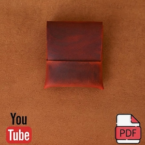May include: A rectangular, dark reddish-brown leather pouch with a smooth, folded flap closure. The leather features a visible grain texture and subtle colour variations, presenting a simple, structured design for holding small items securely.