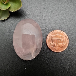 Peut inclure: Une pierre de quartz rose ovale de couleur rose pâle à côté d'une pièce de monnaie américaine d'un cent. La pièce est datée de 1982 et porte l'inscription "United States of America, E Pluribus Unum, One Cent".