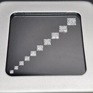 May include: A row of ten clear, square-shaped diamonds of varying sizes, arranged in ascending order from left to right, displayed in a black velvet-lined box.