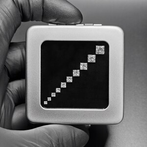 May include: A silver box with a black interior displaying a graduated series of square-shaped diamonds.