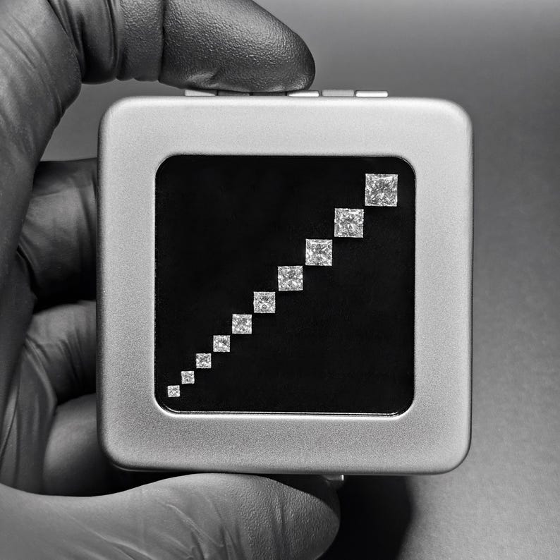 May include: A silver box with a black interior displaying a graduated series of square-shaped diamonds.