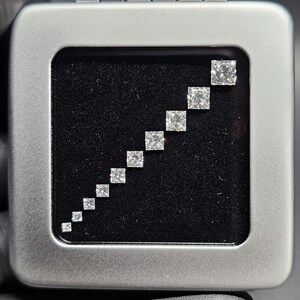 May include: A silver box with a black velvet interior containing a graduated set of square-shaped diamonds.