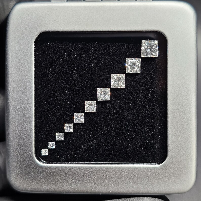 May include: A silver box with a black velvet interior containing a graduated set of square-shaped diamonds.