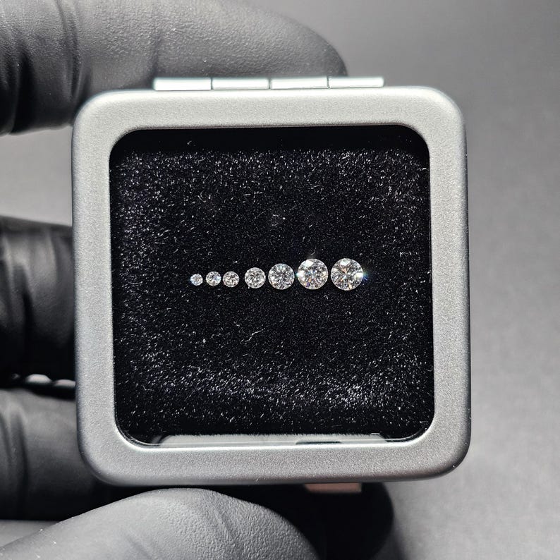 Puede incluir: Una caja gris forrada de terciopelo con una fila de diez diamantes redondos y transparentes de diferentes tama&ntilde;os.