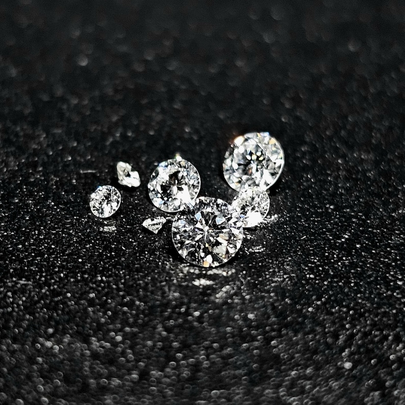 Puede incluir: Un grupo de seis diamantes transparentes, redondos y facetados sobre un fondo negro.