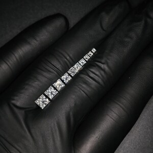May include: A row of clear square-shaped diamonds set in a silver band.