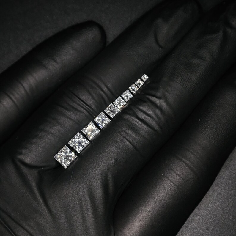May include: A row of clear square-shaped diamonds set in a silver band.
