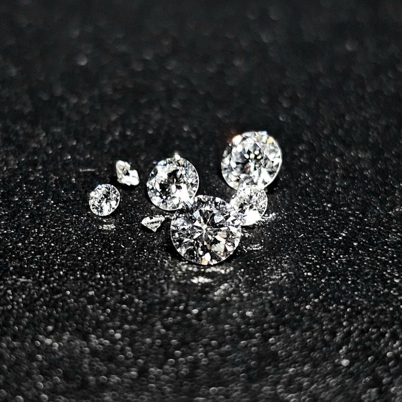 Puede incluir: Un grupo de seis diamantes transparentes, redondos y facetados sobre un fondo negro.