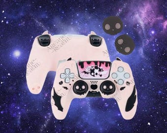 Puede incluir: Un mando de videojuegos rosa claro con detalles negros y una placa frontal decorativa con un diseño en blanco y negro. También se ven dos agarres para el pulgar a juego y un segundo mando sobre un fondo espacial.