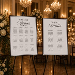 Puede incluir: Dos letreros enmarcados en blanco sobre caballetes negros con el texto "YOUR SEAT Awaits" y los nombres de los invitados organizados por número de mesa. Los letreros están en una habitación bien iluminada con candelabros y arreglos florales.