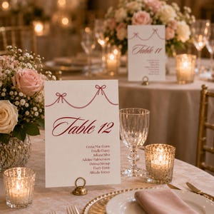 以下が含まれることがあります： 結婚式のテーブルセッティング。花、キャンドル、食器が配置されています。「Table 12」と「Table 11」と書かれたテーブル番号カードが表示されています。カードには名前が記載されており、金色のホルダーで保持されています。