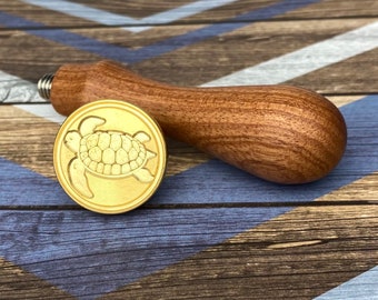 May include: A wooden handle wax seal stamp with a gold-toned metal seal featuring a sea turtle design.