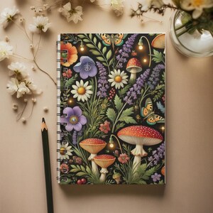 May include: Spiral-bound notebook with a vibrant floral and mushroom design. The cover features colorful flowers, mushrooms, and butterflies against a black background. A pencil rests beside the notebook.